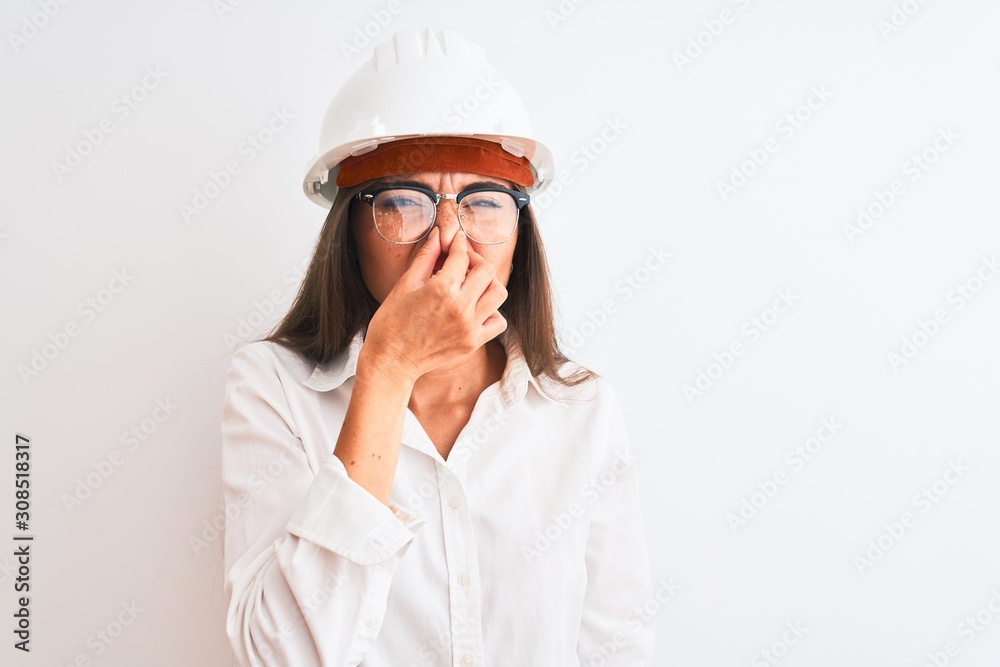 Young beautiful architect woman wearing helmet and glasses over isolated white background smelling something stinky and disgusting, intolerable smell, holding breath with fingers on nose. Bad smell