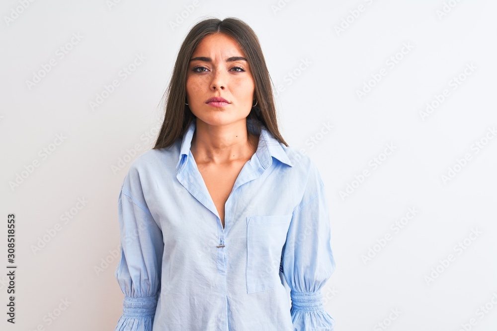 Young beautiful woman wearing blue elegant shirt standing over isolated white background with serious expression on face. Simple and natural looking at the camera. Young beautiful woman wearing blue elegant shirt standing over isolated white background with serious expression on face. Simple and natural looking at the camera.