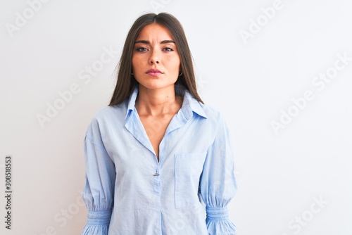 Young beautiful woman wearing blue elegant shirt standing over isolated white background with serious expression on face. Simple and natural looking at the camera.