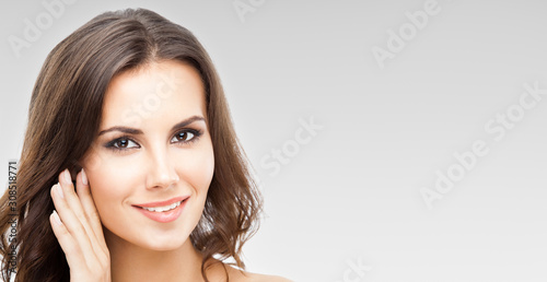 Portrait of nicely smiling woman with long curly hair, over grey background, with copy space for slogan or some text message