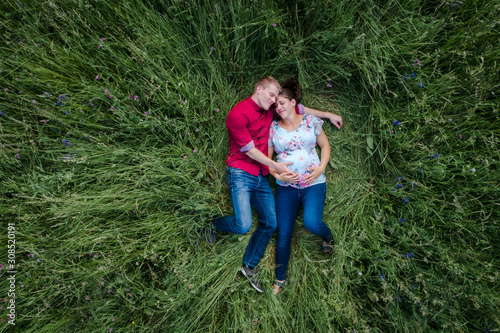 Pregnant woman and man holding baby belly, lying on meadow © Westend61