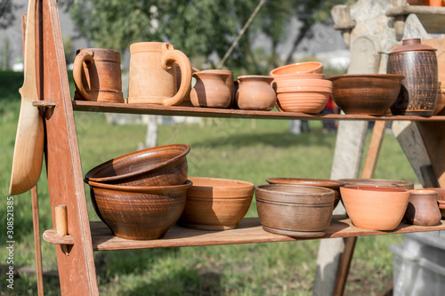 Ceramics fair in Park. Clay dishes on wooden shelf. Pottery craft. Kitchen utensils. Folk art. Everyday life. Household goods © Andrey
