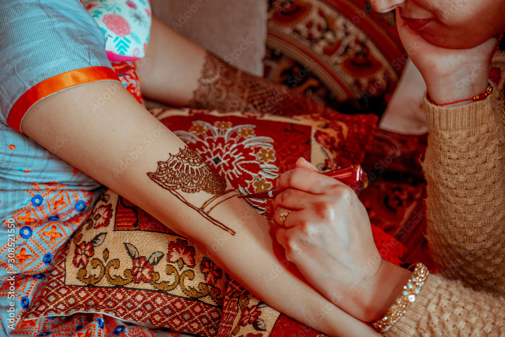 Artist painting traditional indian henna tattoo on woman hand