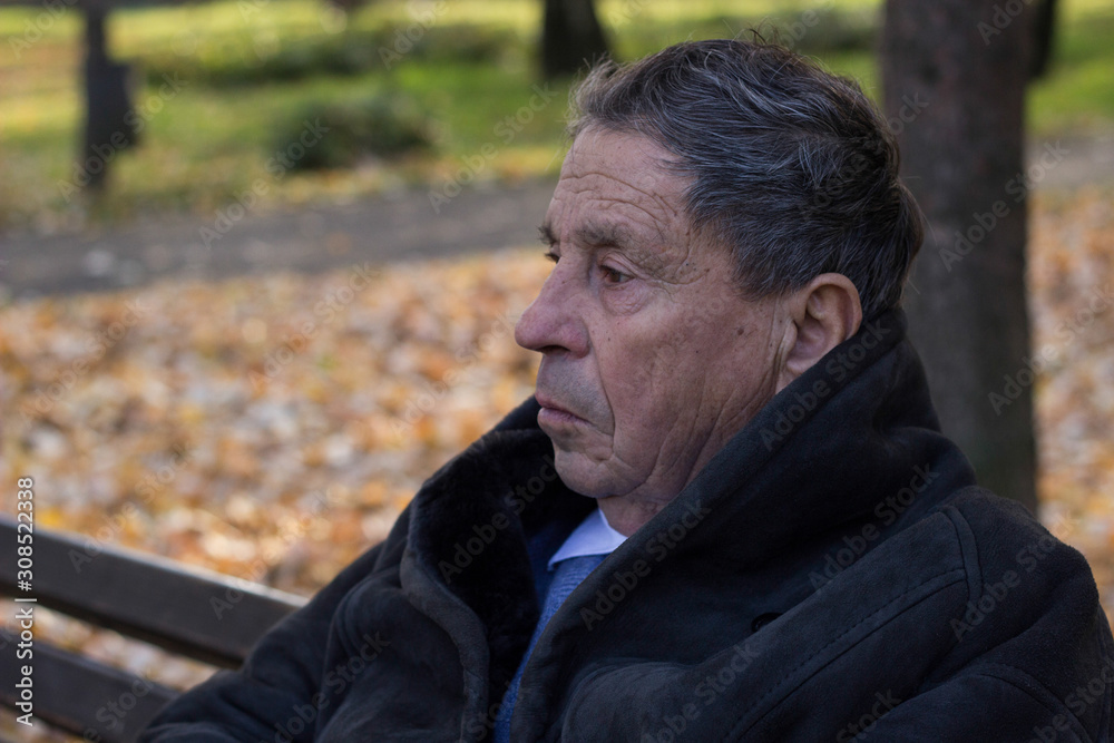 Portrait of a pensive senior man sitting on the bench, in the public park, outdoors. Old man relaxing outdoors and looking away. Portrait of elderly man enjoying retirement Portrait of a pensive senior man sitting on the bench, in the public park, outdoors. Old man relaxing outdoors and looking away. Portrait of elderly man enjoying retirement
