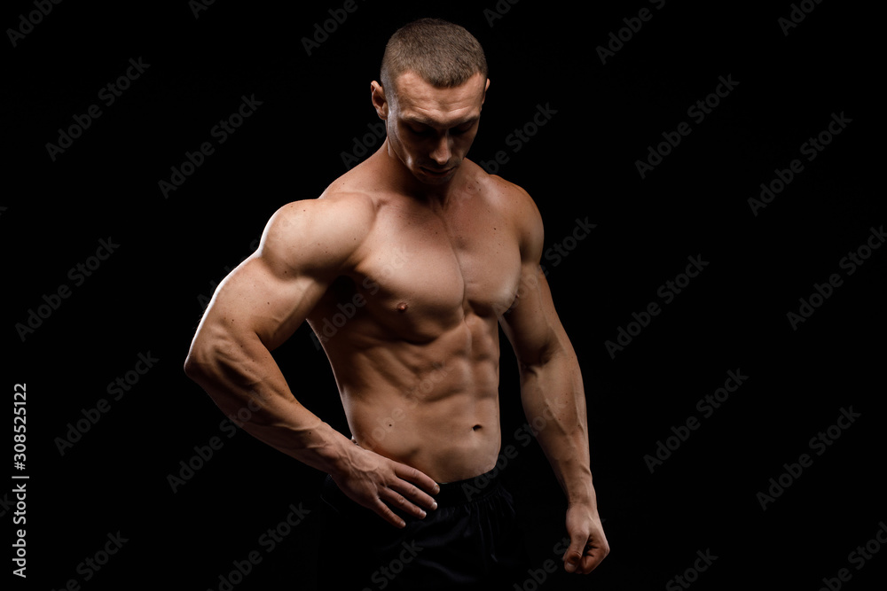 Sexy torso. Muscular model sports young man in jeans showing his press on a black background. Fashion portrait of sporty healthy strong muscle guy. 