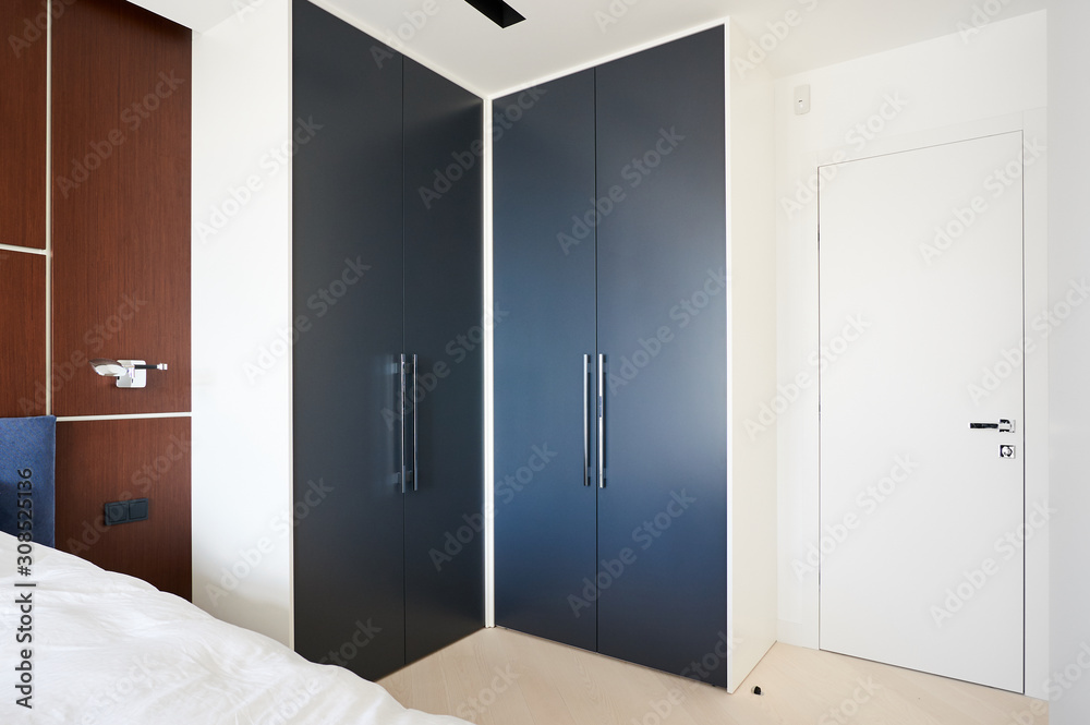 Modern bedroom with fitted wardrobes, a double bed with a cushioned headboard and the wall behind him decorated with veneer walnut Modern bedroom with fitted wardrobes, a double bed with a cushioned headboard and the wall behind him decorated with veneer walnut