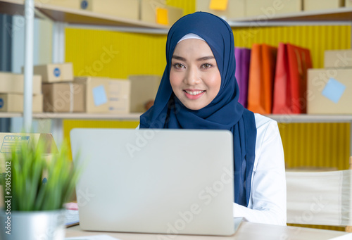 Young asian muslim woman in hijab dress is working at home typing on through laptop.. Small business owner and online marketing and SME concept.