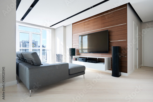 TV area in the modern Hi tech living room: French window, grey corner sofa, acoustic system and solid walnut wall panels