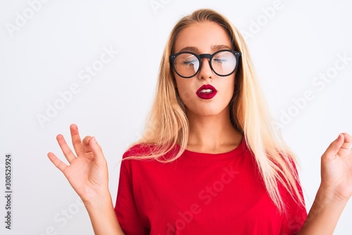 Young beautiful woman wearing red t-shirt and glasses standing over isolated white background relax and smiling with eyes closed doing meditation gesture with fingers. Yoga concept.