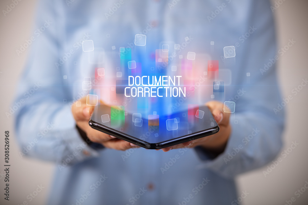 Young man holding a foldable smartphone with DOCUMENT CORRECTION inscription, educational concept Young man holding a foldable smartphone with DOCUMENT CORRECTION inscription, educational concept