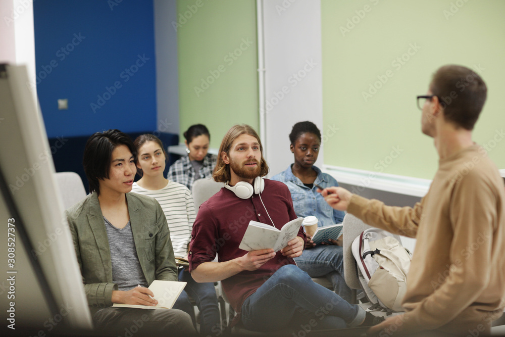 Young people in casual clothing sitting and answering the questions together asked by young teacher at seminar Young people in casual clothing sitting and answering the questions together asked by young teacher at seminar