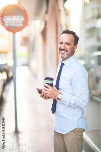 Middle age handsome businessman using smartphone drinking take away coffee smiling