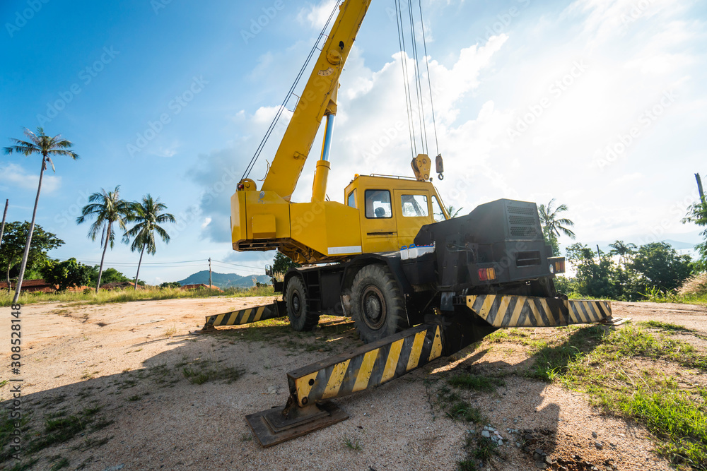 Yellow automobile crane with risen telescopic boom outdoors. Mobile construction crane on a constructin site. Crane machine stand by waiting for work under the construction building. Heavy industry.