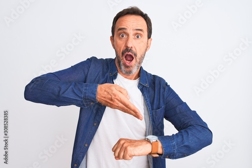 Middle age handsome man wearing blue denim shirt standing over isolated white background In hurry pointing to watch time, impatience, upset and angry for deadline delay