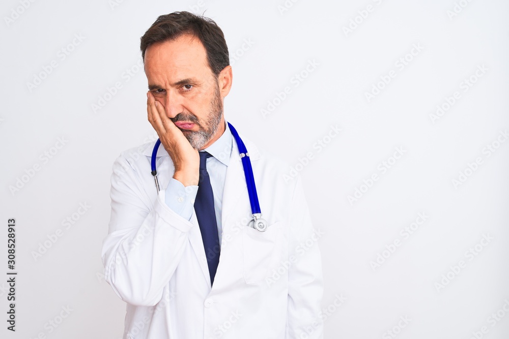 Middle age doctor man wearing coat and stethoscope standing over isolated white background thinking looking tired and bored with depression problems with crossed arms. Middle age doctor man wearing coat and stethoscope standing over isolated white background thinking looking tired and bored with depression problems with crossed arms.