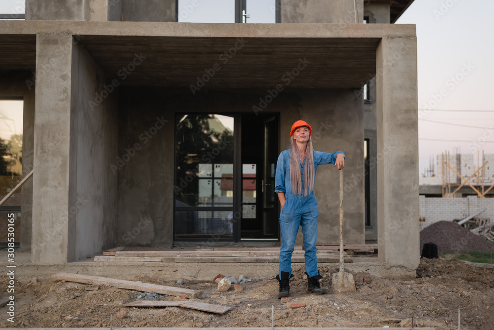 Woman worker with a shovel stands at a construction site. Background