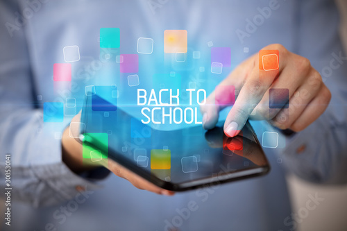 Young man holding a foldable smartphone with BACK TO SCHOOL inscription, educational concept
