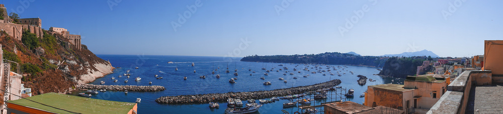 Panoramic view of beautiful Procida on a sunny summer day. Colorful cafes, houses and restaurants, fishing boats and yachts, clear blue sky and the azure sea on the island of Procida, Italy. Napoli