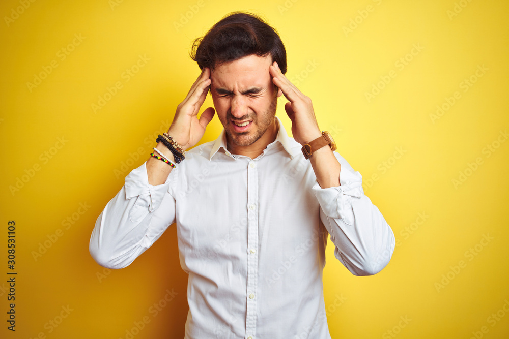 Young handsome businessman wearing elegant shirt standing over isolated yellow background with hand on head for pain in head because stress. Suffering migraine.