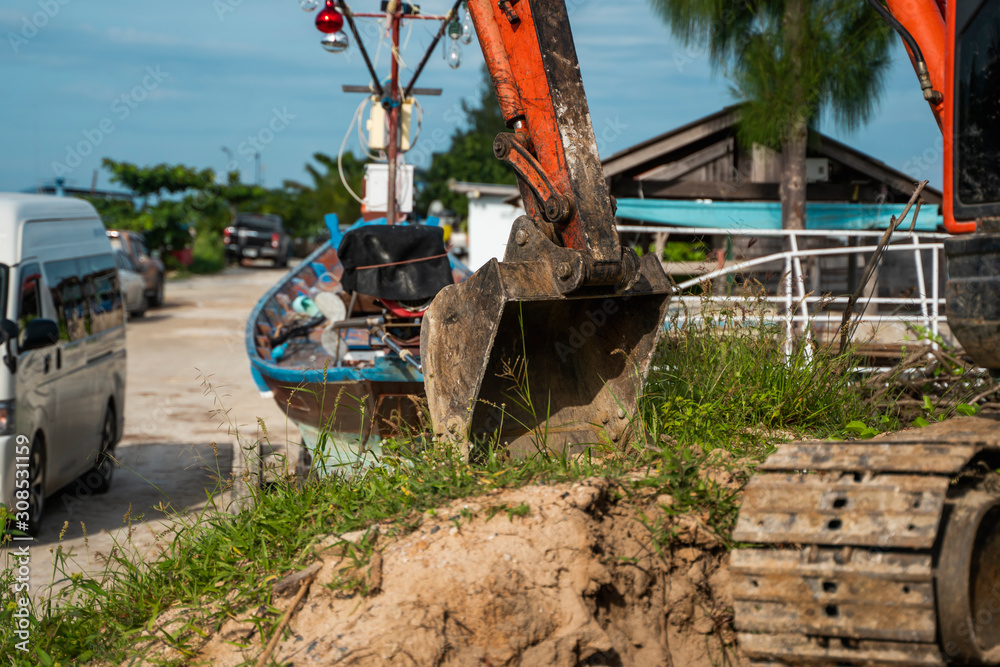 Fototapeta premium Small orange excavator on a ground against blue sky and sea for a works on construction site. Small tracked excavator standing on a ground with a blue sea on background. Heavy industry.
