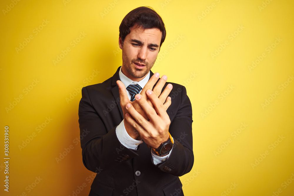 Young handsome businessman wearing suit and tie standing over isolated yellow background Suffering pain on hands and fingers, arthritis inflammation Young handsome businessman wearing suit and tie standing over isolated yellow background Suffering pain on hands and fingers, arthritis inflammation