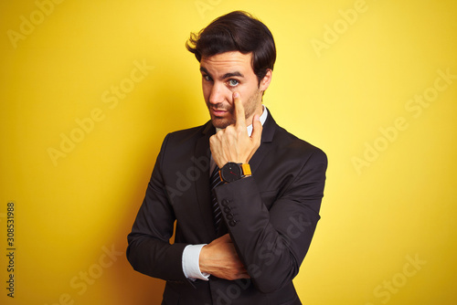 Young handsome businessman wearing suit and tie standing over isolated yellow background Pointing to the eye watching you gesture, suspicious expression