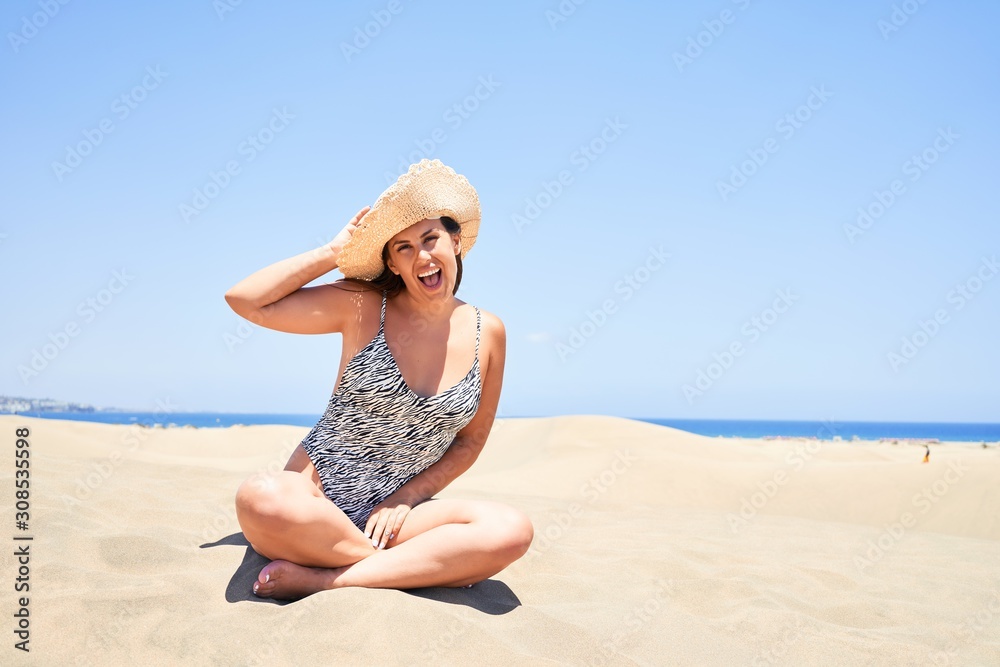 Young beautiful woman sunbathing sitting on the sand wearing summer swinsuit at maspalomas dunes bech Young beautiful woman sunbathing sitting on the sand wearing summer swinsuit at maspalomas dunes bech