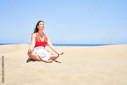 Young beautiful woman sunbathing and relaxing sitting on the sand doing yoga poses at maspalomas dunes bech