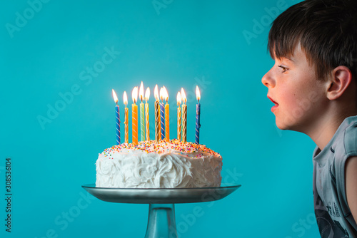 Boy ready to blow out candles on birthday cake against blue backdrop.