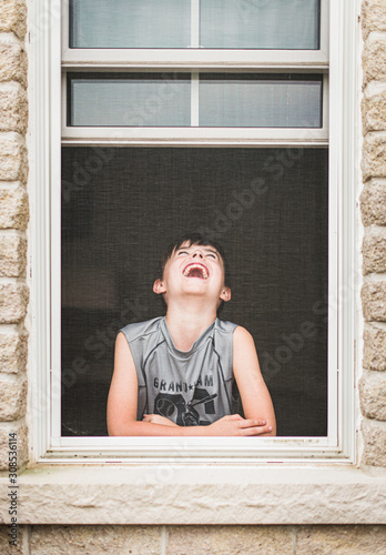 Young boy laughing in an open window shot through the screen. photo