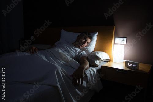 A man with insomnia looks at the clock at dawn from the bed with concern