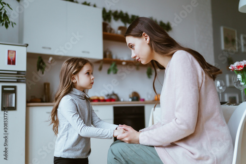 mom with a little daughter in the kitchen. the girl tells something and mom listens carefully to her