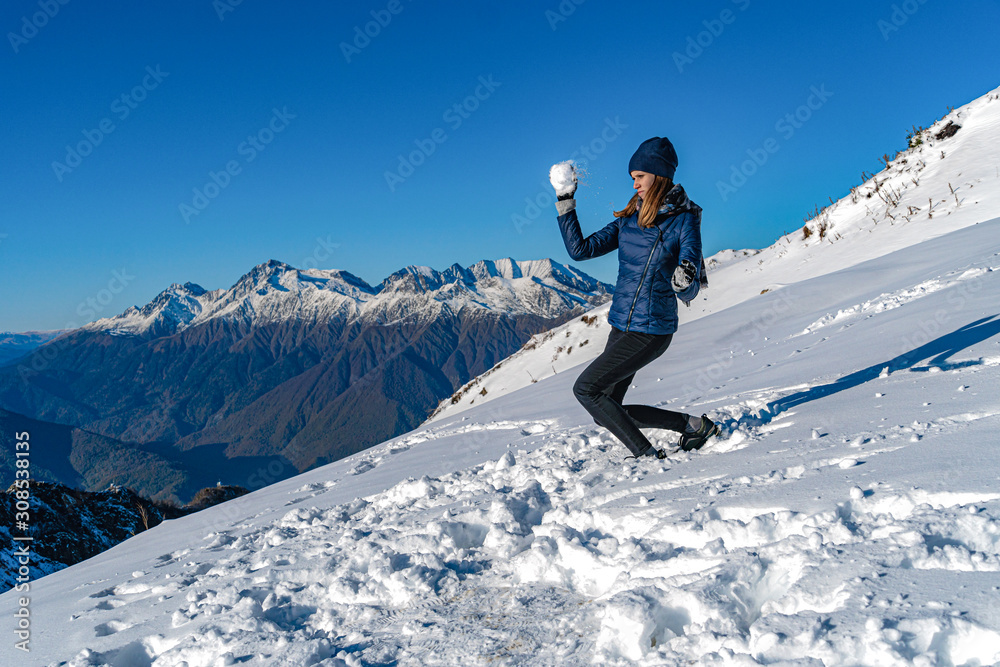 Young woman throwing snowball at sunny day at mountains