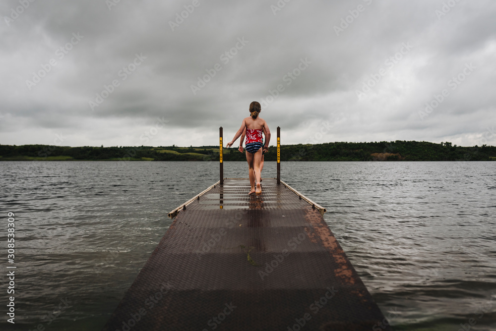 Little Girls Walk on Dock Toward Water on a Cloudy Day at the Lake Little Girls Walk on Dock Toward Water on a Cloudy Day at the Lake