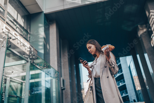 A girl with a pie in her hand looks anxiously at the phone on a city street