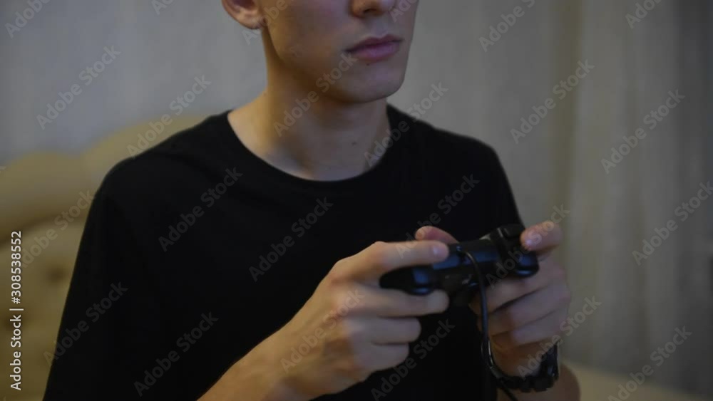 Young man smiles and enjoys winning with gamepad in hand, playing video games console, siting on the bed. Young man smiles and enjoys winning with gamepad in hand, playing video games console, siting on the bed.