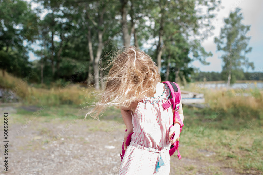 young blonde girl putting a backpack on with the wind blowing her hair young blonde girl putting a backpack on with the wind blowing her hair