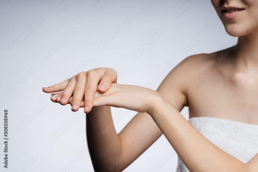 Fototapeta premium in the frame, beautiful female hands with delicate skin make movements as if rubbing cream, the girls chin and naked shoulder are visible. gray background