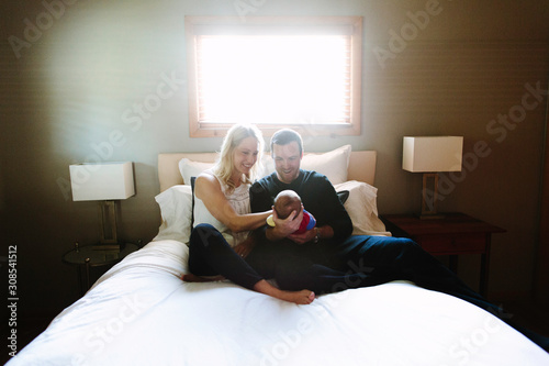 Two new parents smile at their newborn son while sitting on a bed