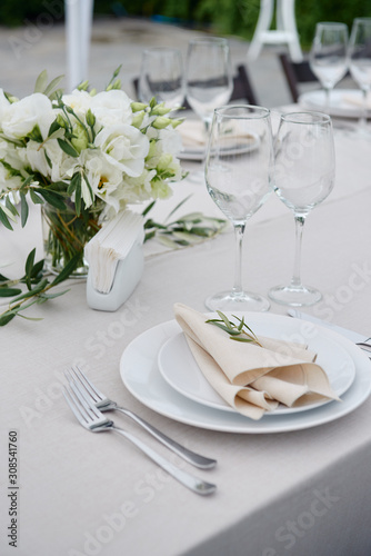 Table setting with beige napkin on empty white plate, wineglasses and cutlery on table, copy space. Place setting at wedding reception. Table served for banquet