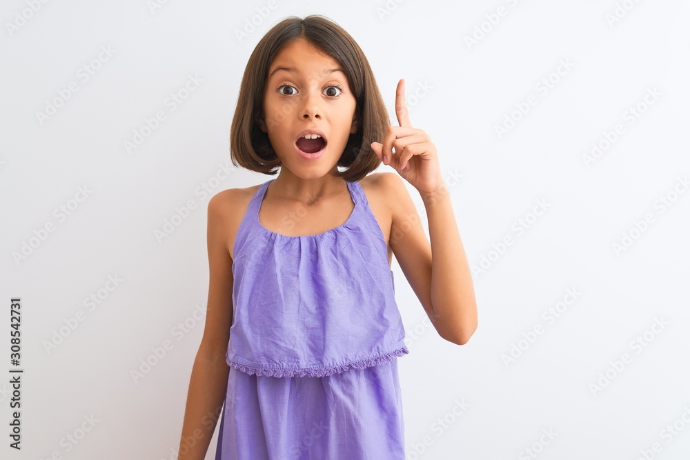 Young beautiful child girl wearing purple casual dress standing over isolated white background pointing finger up with successful idea. Exited and happy. Number one. Young beautiful child girl wearing purple casual dress standing over isolated white background pointing finger up with successful idea. Exited and happy. Number one.