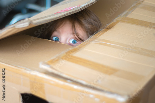 Guilty baby hid from parents and is afraid. A scared little girl peeks out of a cardboard shelter. The child is sitting inside the mail box and is afraid. photo