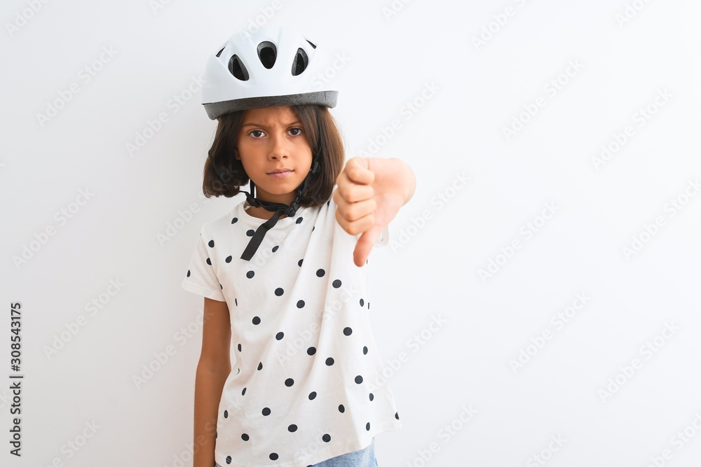 Beautiful child girl wearing security bike helmet standing over isolated white background looking unhappy and angry showing rejection and negative with thumbs down gesture. Bad expression. Beautiful child girl wearing security bike helmet standing over isolated white background looking unhappy and angry showing rejection and negative with thumbs down gesture. Bad expression.