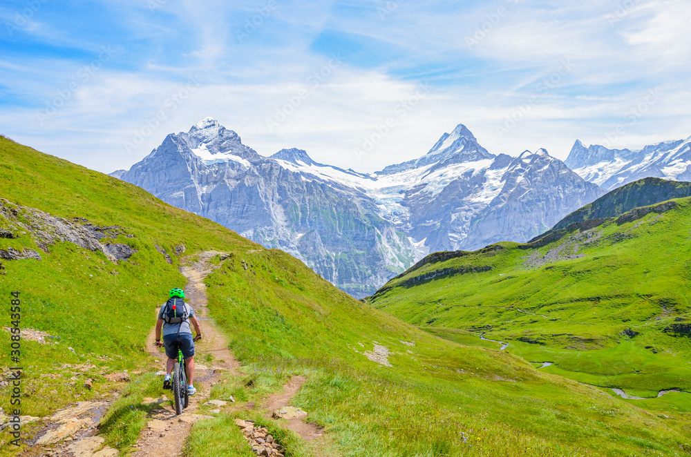 Mountain biker riding downhill the beautiful summer Alpine landscape. Snowcapped mountains in the background. Photographed on the trail from Grindelwald to Bachalpsee. Active vacation