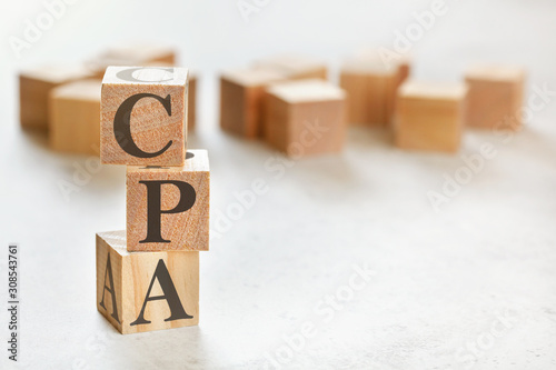 Three wooden cubes with letters CPA (means Cost per action / acquisition), on white table, more in background, space for text in right down corner