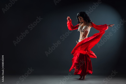 beautiful black-haired girl in red ethnic dress on the stage dancing oriental dance waving her skirt