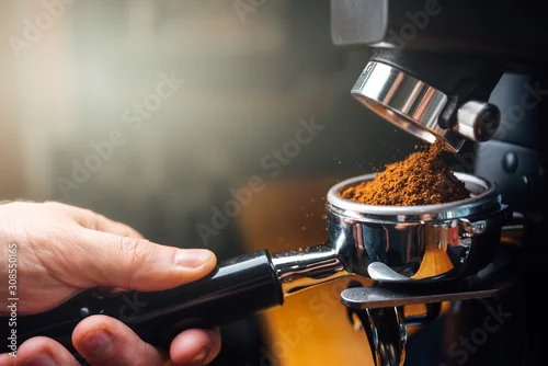 Obraz ground coffee pouring into a portafilter with a grinder