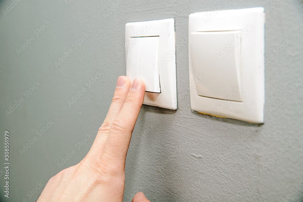 The hand presses the light switch. The concept of saving electricity, turning on the light in dark days. The hand presses the light switch. The concept of saving electricity, turning on the light in dark days.