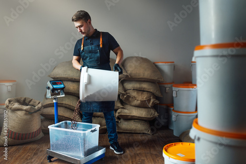 Obraz na plátně a worker in a uniform pours roasted coffee from a white bucket into a transparen