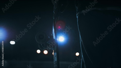 Feet and Board close-up: a young guy stands with a skateboard in his hand on a dark night on the street in the light of lanterns. Skateboarder with a skate. Rear and bottom view, slow motion, 4K
